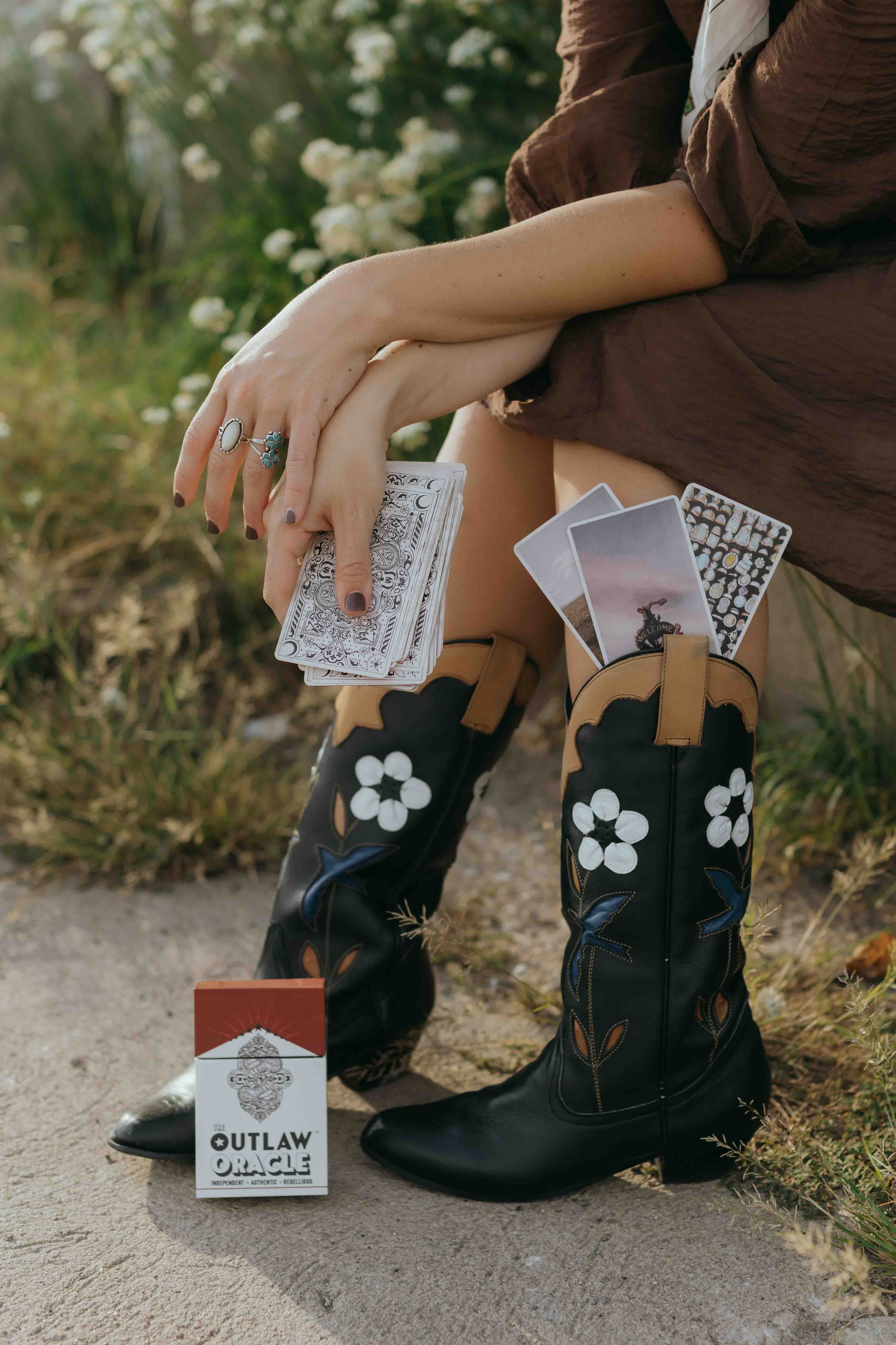 Outlaw Oracle cards and card deck styled with Western Fashion - showing the nostalgic red and white American Western inspired box that the oracle deck comes in, and the high quality oracle card stock in hand. Beautiful quality and finish. Looks great on your coffee table.