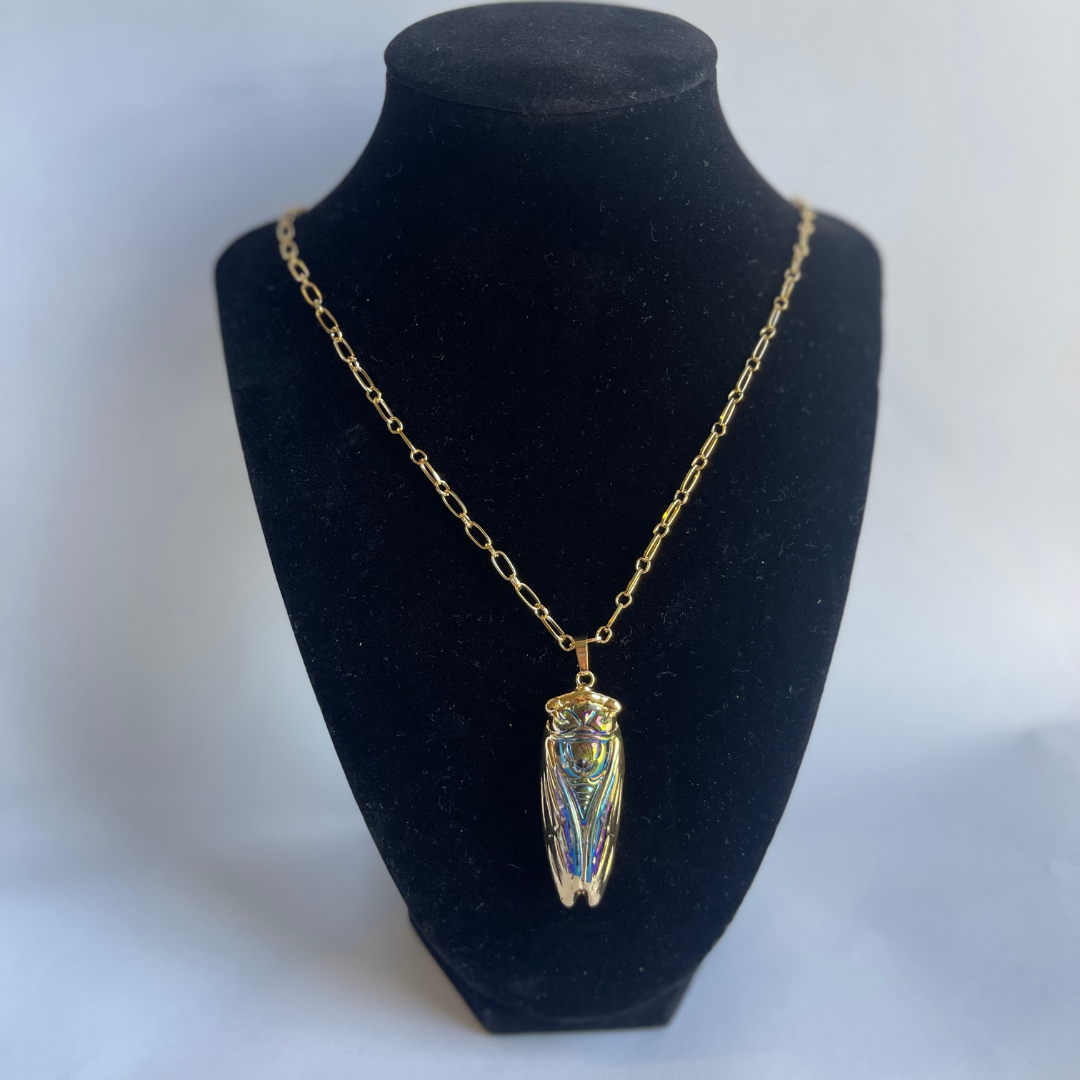 Display of iridescent glass cicada pendant showing rainbow light effects and gold accents